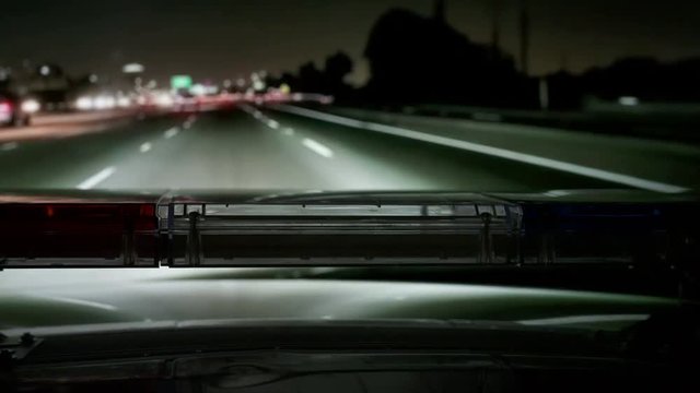 POV Police highway patrol car with red blue flash emergency lights driving on freeway at night.