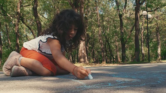 A child girl draws on the asphalt. A little girl draws chalk in the park. 4k slow motion