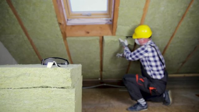 Man installing thermal roof insulation layer - using mineral wool panels. Attic renovation and insulation concept