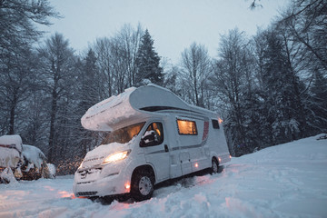 camping car or campervan outdoor on the mountain side offroad near the forest in the winter snowing