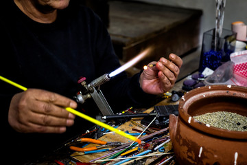 Obraz premium a glassblower man made Handicraft from melted glass in glassblowing workshop. Glass art is shaping at the end of glassblowing pipe. 