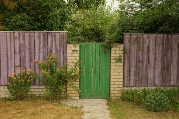 part of a rural wooden fence and a closed green door in the grass and branches