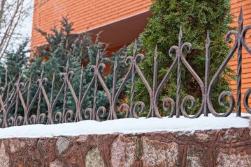 part of a stone fence with gray iron sharp rods in the snow