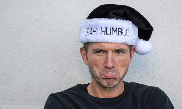 pouting Caucasian man wearing a black and white fur hat displaying the words Bah Humbug on the brim, with copy space
