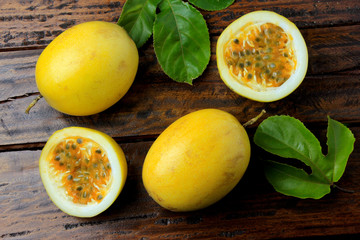 yellow passion fruit with leaves and passion fruit cut in half on rustic wooden table