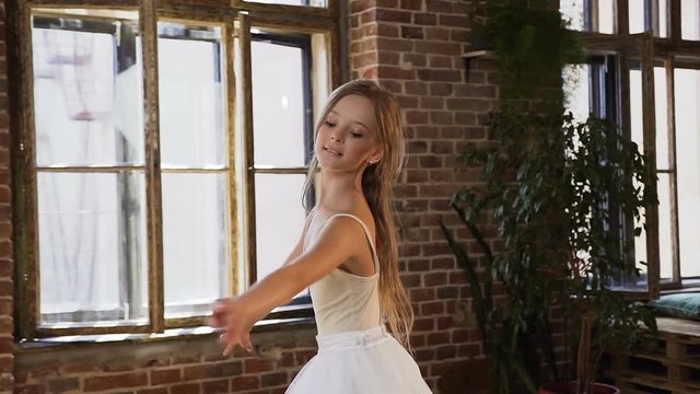 Professional ballet dancer dressed in white tutu perform classic ballet dance, she trains gracefully in pointe ballet shoes. Graceful charming ballerina practicing ballet movements at the dance-hall