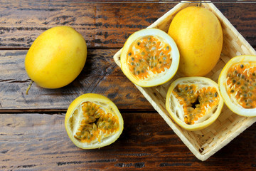 yellow passion fruit and passion fruit cut in half in basket on wooden table.