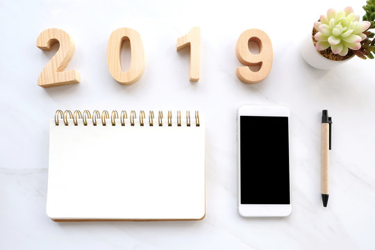 2019 wood letters, blank notebook paper, white smart phone with blank screen and pencil on white marble table background, 2019 new year mock up, template with copy space for text, top view