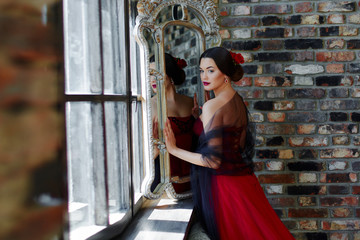 Portrait of a beautiful young woman dancer in a red dress near the window.
