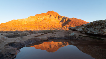 Rainwater in a small pool on top of a sandstone boulder reflects Gooseberry mesa in the last light of a winter day.