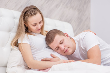 young man listening to the belly of his pregnant wife on the bed