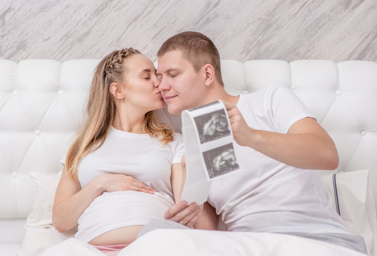 Pregnant woman and her young husband looking at ultrasound scan photo of unborn child
