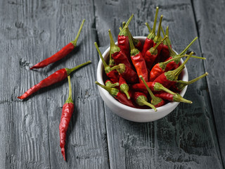 Three chilli pods and a white bowl of peppers on a dark wooden table. The view from the top.