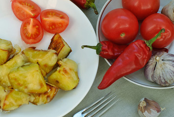 Fried potatoes on a white plate, tomatoes, red peppers and garlic. Top view.