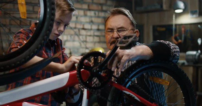 Medium shot of grandfather and grandson repairing a bicycle in a garage