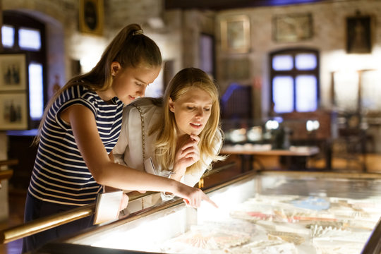 Girl with woman looking with interest at art objects under glass in museum