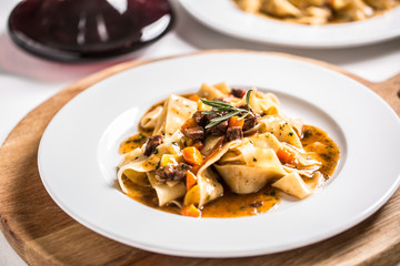 Idalian pasta pappardelle with beef ragu on white plate and red wine