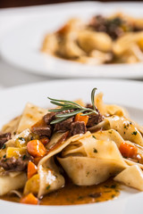 Idalian pasta pappardelle with beef ragout on white plate.