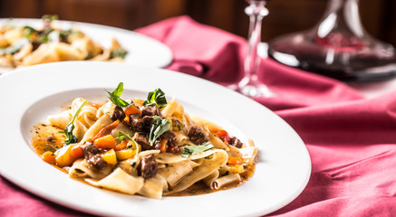 Idalian pasta pappardelle with beef ragout on white plate and red wine