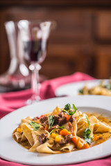 Idalian pasta pappardelle with beef ragout on white plate and red wine
