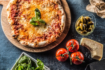 Italian traditional pizza margarita on round wooden board with basil tomatoes and parmesan