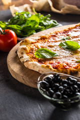 Italian traditional pizza margarita on round wooden board with basil tomatoes and parmesan
