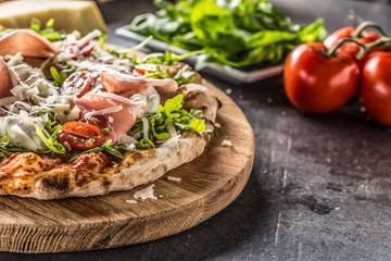 Italian pizza with prosciutto arugula tomatoes and parmesan on wooden round board