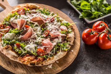 Italian pizza with prosciutto arugula tomatoes and parmesan on wooden round board