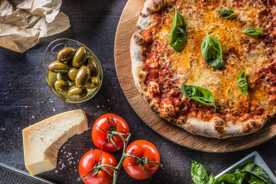 Italian traditional pizza margarita on round wooden board with basil tomatoes and parmesan