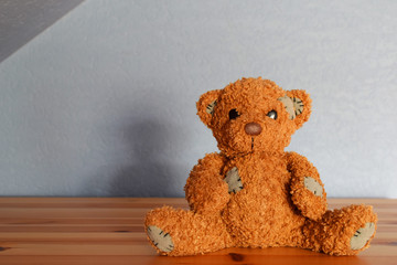 Cute little brown teddy bear plush toy sitting on wooden shelf on blue wall background with copy space for text.
