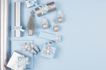 Modern soft minimalist christmas background with copy space - pastel blue and silver metallic gift boxes with shiny ribbons and bows on blue color backdrop, top view.
