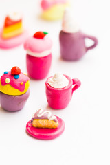 Miniature play dough coffee or latte cup with cream topping, piece of cake on pink plate, white isolated background, artificial food concept, kids craft sculpture, mini art, copy space, coffee shop