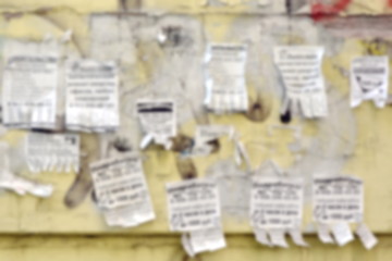 Live bulletin board. Shreds of various ads on an old yellow wall. Blurred background
