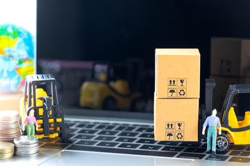 Mini forklift truck load cardboard boxes with symbol and stack of coins on laptop keyboard with globe near by. Logistics and transportation management ideas and Industry business commercial concept.