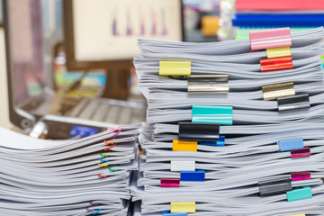 Pile of unfinished documents on office desk. Stack of homework assignment archive with colorful clips and slide binder bars on teacher table waiting to be managed. Education and business concept.