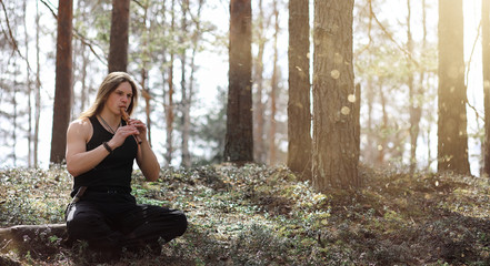 A musician with a tool in nature. A man is playing a flute in a pine forest. The music of the...
