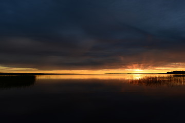 Fototapeta na wymiar Twilight glow of sunlight in the gloomy sky above the water of the lake