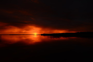 Nightfall sky in the twilight light of the setting sun in bright red colors on a dark background of the lake water