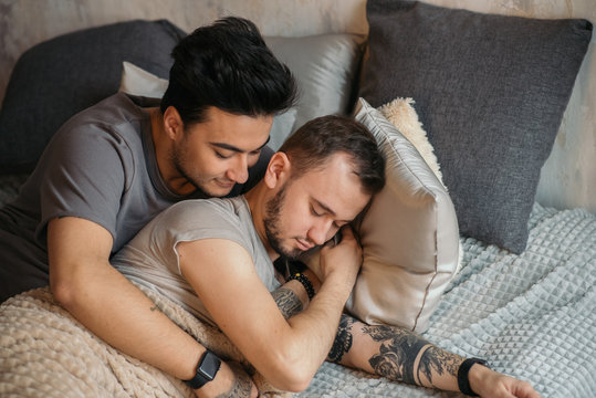 Caucasian homosexual family in bed before sleep. Handsome hot man with bristle kissing good night his sleepy male partner, lying in bed