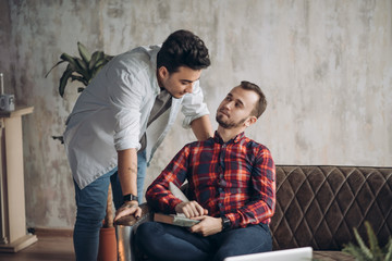 European homosexual male couple enjoying leisure time together, sitting by table and watching online movie on laptop computer in the living room with monochrome interior