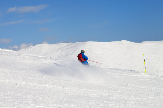 Skier downhill on snowy ski slope in sun winter day