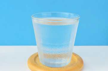 glass of cold water on wooden coaster against blue background