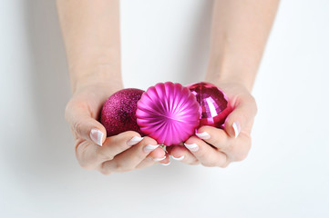 Two women's hands hold three Christmas tree decorations in the form of balls. Nails on hands with french manicure. Close-up. White background.