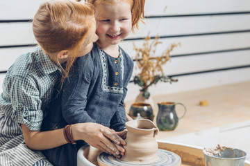 eleder sister kissing her little sister while creating a clay vase. close up photo. copy space