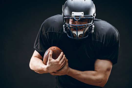 American football sportsman player in black outfit and helmet runing, isolated on black background