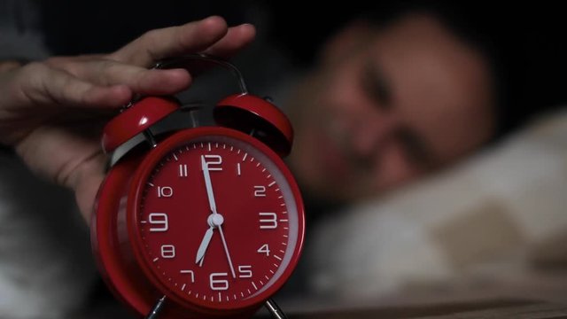 Young man stopping the clock alarm early in the morning