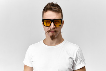 Style, fashion and optics concept. Portrait of handsome fashionable young Caucasian male posing in studio wearing white t-shirt and yellow rectangular eyeglasses, having serious confident look