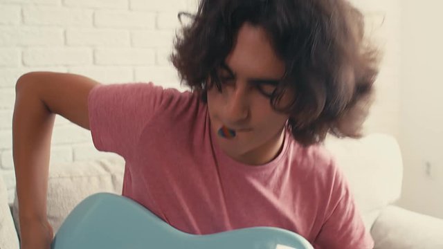 Teenager boy is sitting on bed at home and playing guitar, 4k