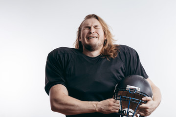 Young handsome rugby player with long hair over isolated background holding helmet under his arm,...