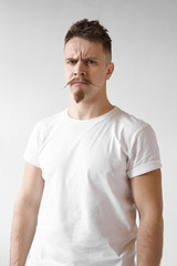 Grumpy hipster man with stylish mustache and beard frowning and staring at camera with angry facial expression, being dissatisfied with quality of product or service. Negative human reaction